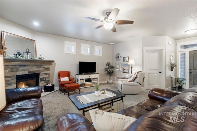 living room featuring ceiling fan, a stone fireplace, and carpet