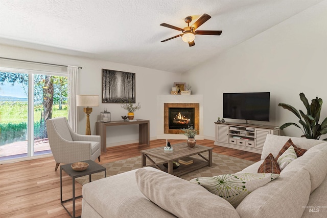 living room featuring light wood-type flooring, a textured ceiling, vaulted ceiling, ceiling fan, and a tile fireplace