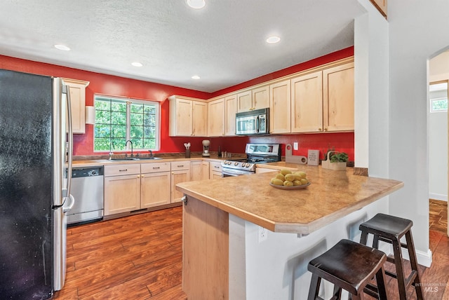 kitchen featuring sink, stainless steel appliances, kitchen peninsula, a breakfast bar, and light wood-type flooring