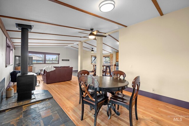 dining area featuring a wood stove, ceiling fan, wood-type flooring, and baseboards