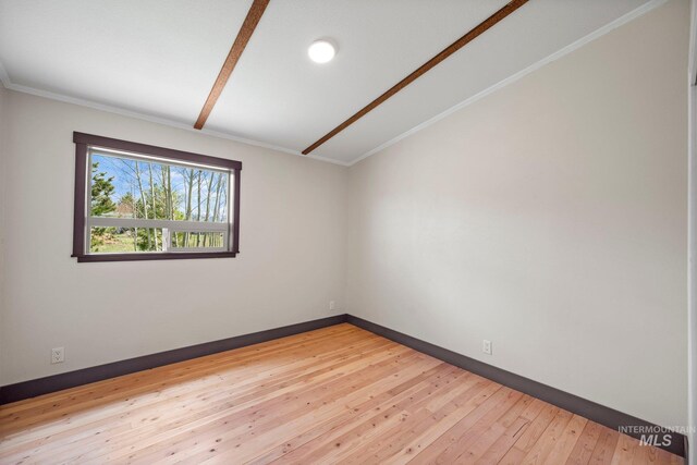 empty room featuring vaulted ceiling, light wood-type flooring, baseboards, and ornamental molding
