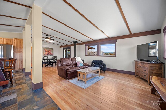 living room with baseboards, ceiling fan, a wood stove, and wood-type flooring