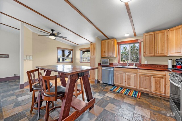 kitchen with appliances with stainless steel finishes, stone tile floors, dark countertops, a sink, and lofted ceiling
