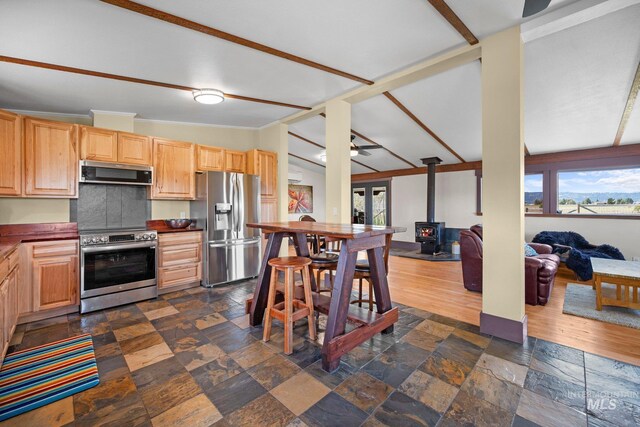 kitchen featuring appliances with stainless steel finishes, a wood stove, healthy amount of natural light, open floor plan, and vaulted ceiling