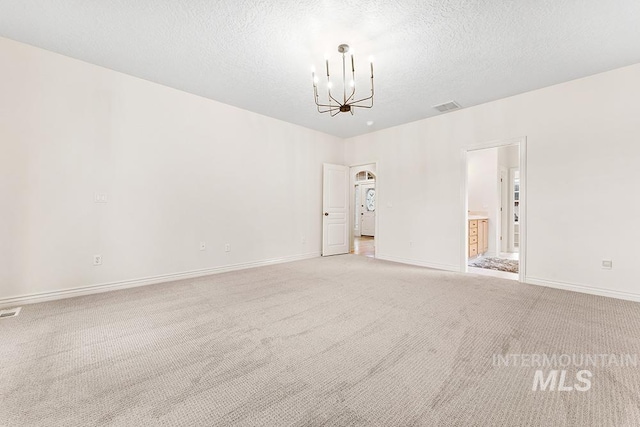 unfurnished room featuring light colored carpet, a textured ceiling, and an inviting chandelier