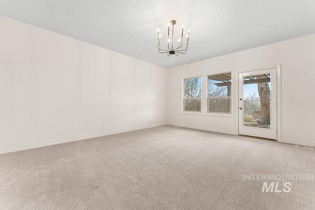 carpeted spare room with a notable chandelier and a textured ceiling