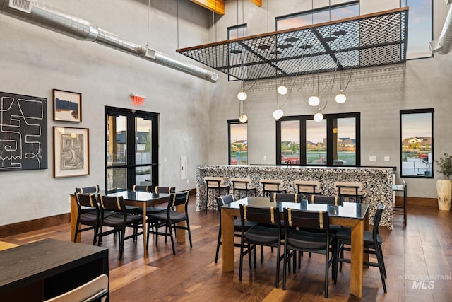 dining area featuring hardwood / wood-style flooring, a towering ceiling, and french doors