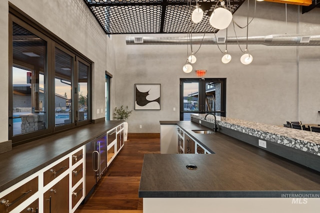 kitchen with dark wood-type flooring, french doors, sink, hanging light fixtures, and a towering ceiling