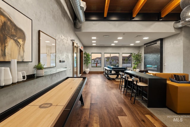 game room featuring a barn door, dark wood-type flooring, and beam ceiling