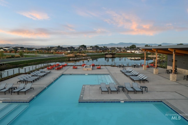 pool at dusk with a water and mountain view and a patio area