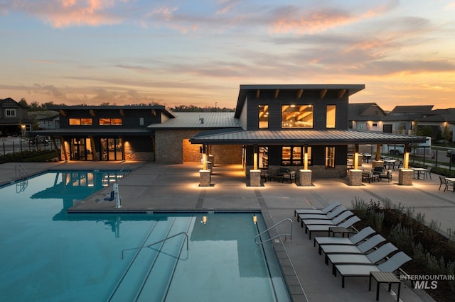 pool at dusk featuring an outdoor bar and a patio