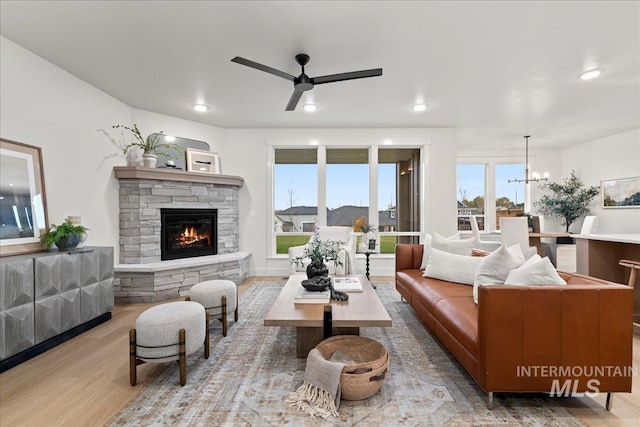 living room featuring ceiling fan with notable chandelier, light hardwood / wood-style flooring, and a stone fireplace