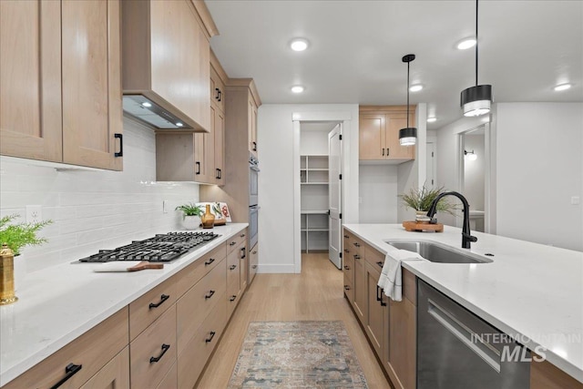 kitchen with appliances with stainless steel finishes, sink, hanging light fixtures, light stone counters, and custom range hood