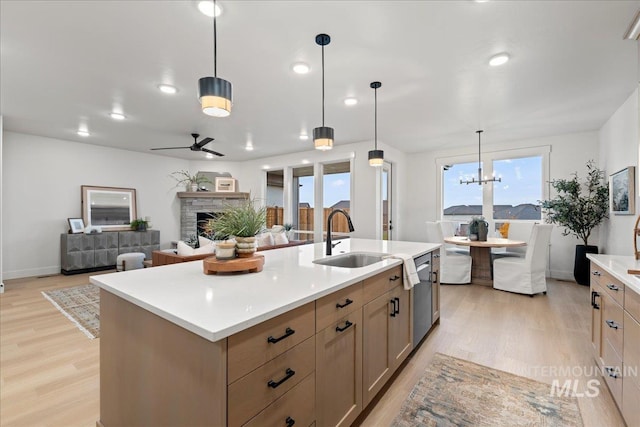 kitchen featuring decorative light fixtures, sink, a stone fireplace, and a center island with sink