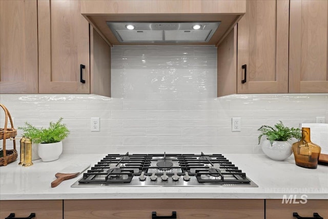 room details featuring light stone countertops, stainless steel gas cooktop, wall chimney exhaust hood, and tasteful backsplash