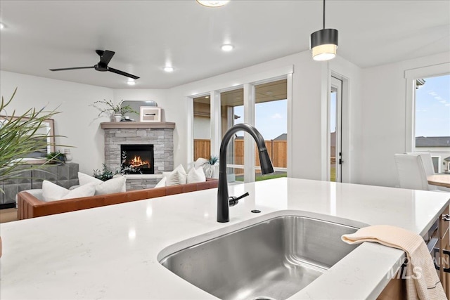 room details with hanging light fixtures, ceiling fan, sink, and a stone fireplace