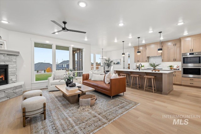 living room with light wood-type flooring, ceiling fan, a stone fireplace, and sink