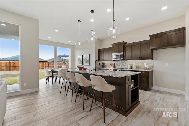 kitchen with light wood-style floors, stainless steel microwave, tasteful backsplash, and dark brown cabinetry