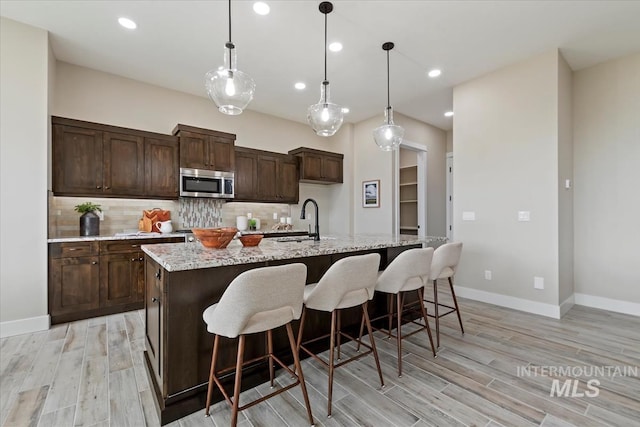 kitchen featuring a sink, stainless steel microwave, backsplash, and light wood finished floors