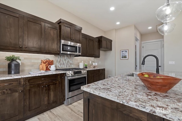 kitchen with pendant lighting, a sink, backsplash, appliances with stainless steel finishes, and dark brown cabinets