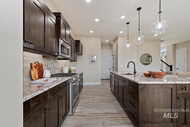 kitchen with tasteful backsplash, dark brown cabinets, light stone countertops, stainless steel appliances, and a sink