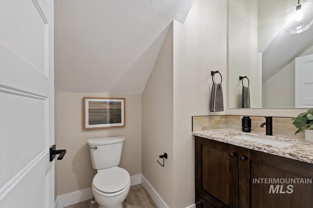 bathroom featuring toilet, wood finished floors, baseboards, vanity, and vaulted ceiling