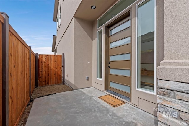 entrance to property featuring a patio area, fence, and stucco siding