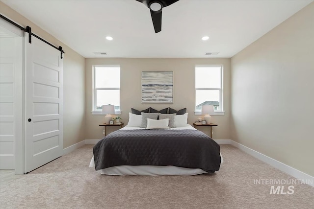 bedroom featuring a barn door, visible vents, baseboards, and carpet