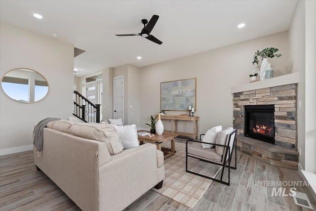 living room with wood finished floors, stairway, a stone fireplace, baseboards, and ceiling fan