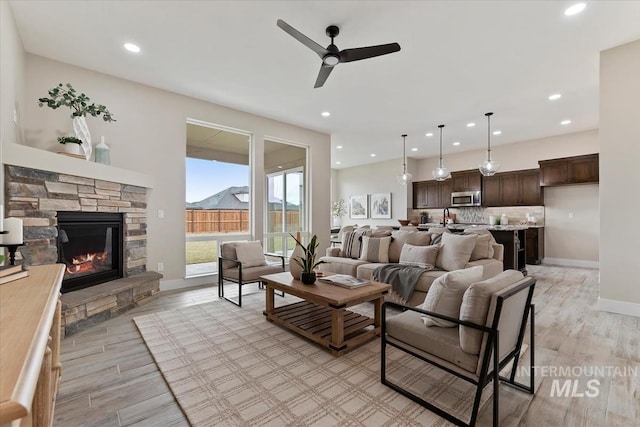 living room featuring light wood finished floors, a fireplace, baseboards, and a ceiling fan