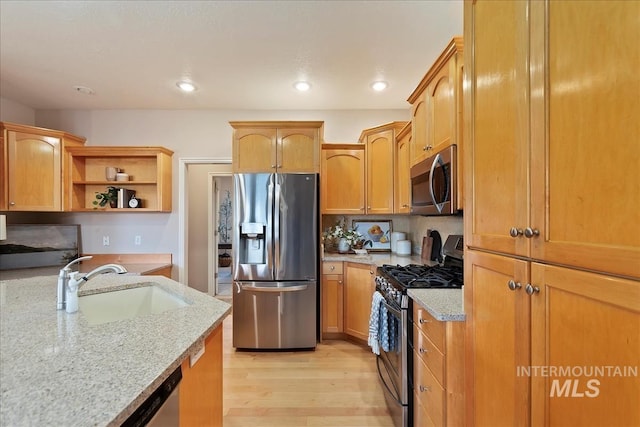 kitchen with light stone counters, light wood finished floors, open shelves, a sink, and stainless steel appliances