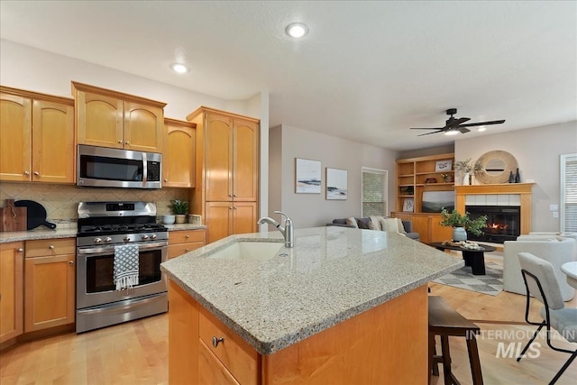 kitchen with an island with sink, a sink, open floor plan, appliances with stainless steel finishes, and a breakfast bar area