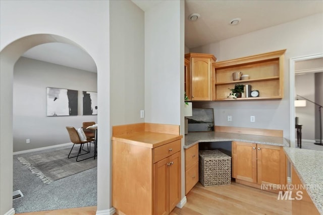 kitchen with light wood-style flooring, open shelves, arched walkways, baseboards, and light colored carpet