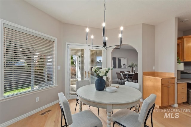 dining room featuring visible vents, light wood finished floors, baseboards, an inviting chandelier, and arched walkways