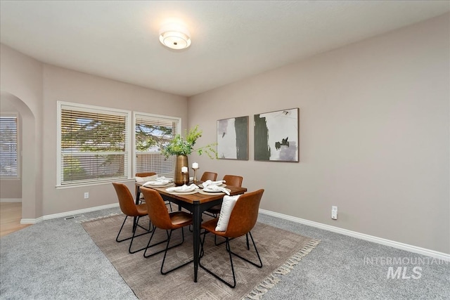 dining area featuring arched walkways, light colored carpet, and baseboards