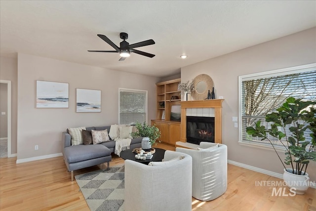 living room with light wood-style flooring, baseboards, ceiling fan, and a fireplace