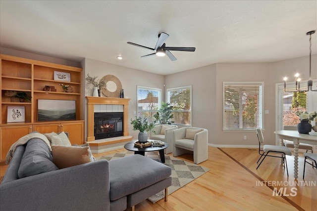 living area with ceiling fan with notable chandelier, a fireplace, light wood-type flooring, and baseboards