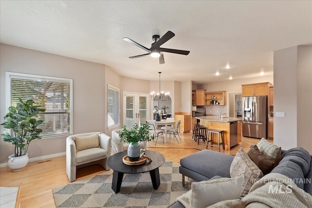 living room with visible vents, baseboards, light wood-style floors, and ceiling fan with notable chandelier