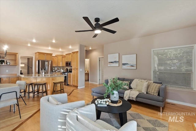 living area featuring light wood-style floors, baseboards, and ceiling fan