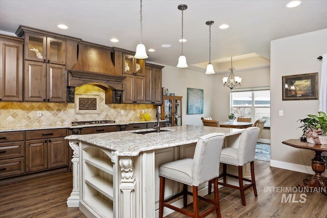 kitchen featuring custom exhaust hood, a kitchen island with sink, sink, dark hardwood / wood-style floors, and decorative backsplash