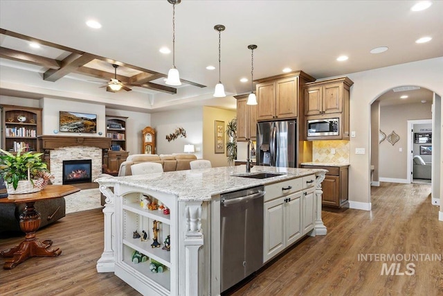 kitchen featuring sink, stainless steel appliances, coffered ceiling, beamed ceiling, and a center island with sink