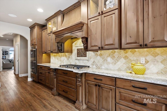 kitchen featuring appliances with stainless steel finishes, dark hardwood / wood-style flooring, backsplash, light stone counters, and custom range hood