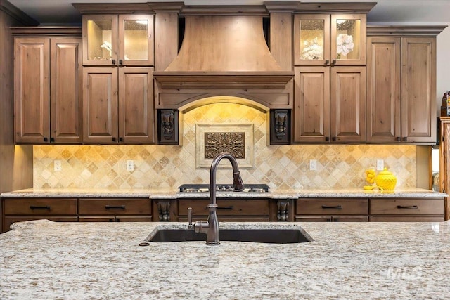 kitchen with light stone countertops, decorative backsplash, sink, and custom exhaust hood