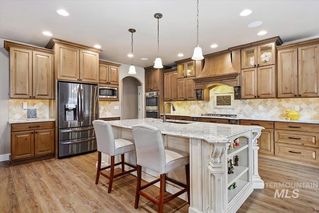 kitchen with custom exhaust hood, sink, hanging light fixtures, an island with sink, and appliances with stainless steel finishes