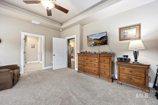 bedroom featuring a raised ceiling, ceiling fan, light colored carpet, and connected bathroom