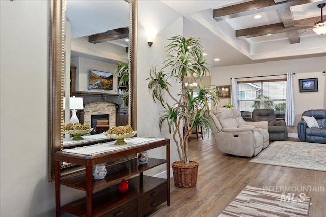 living room with ceiling fan, coffered ceiling, a stone fireplace, beamed ceiling, and hardwood / wood-style flooring