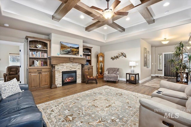 living room featuring beam ceiling, a stone fireplace, hardwood / wood-style floors, and coffered ceiling