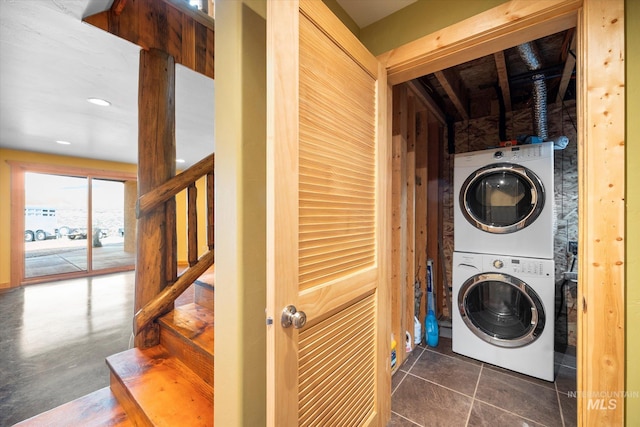 laundry room with dark tile flooring and stacked washer and dryer