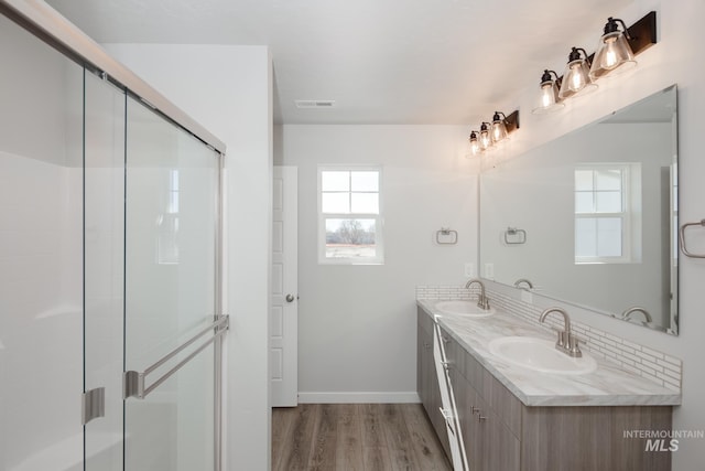 full bath featuring a sink, wood finished floors, a shower stall, double vanity, and baseboards
