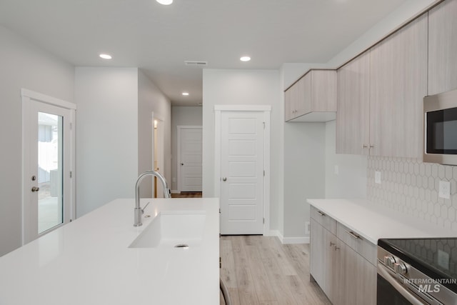 kitchen with stainless steel appliances, light wood finished floors, a sink, light countertops, and tasteful backsplash